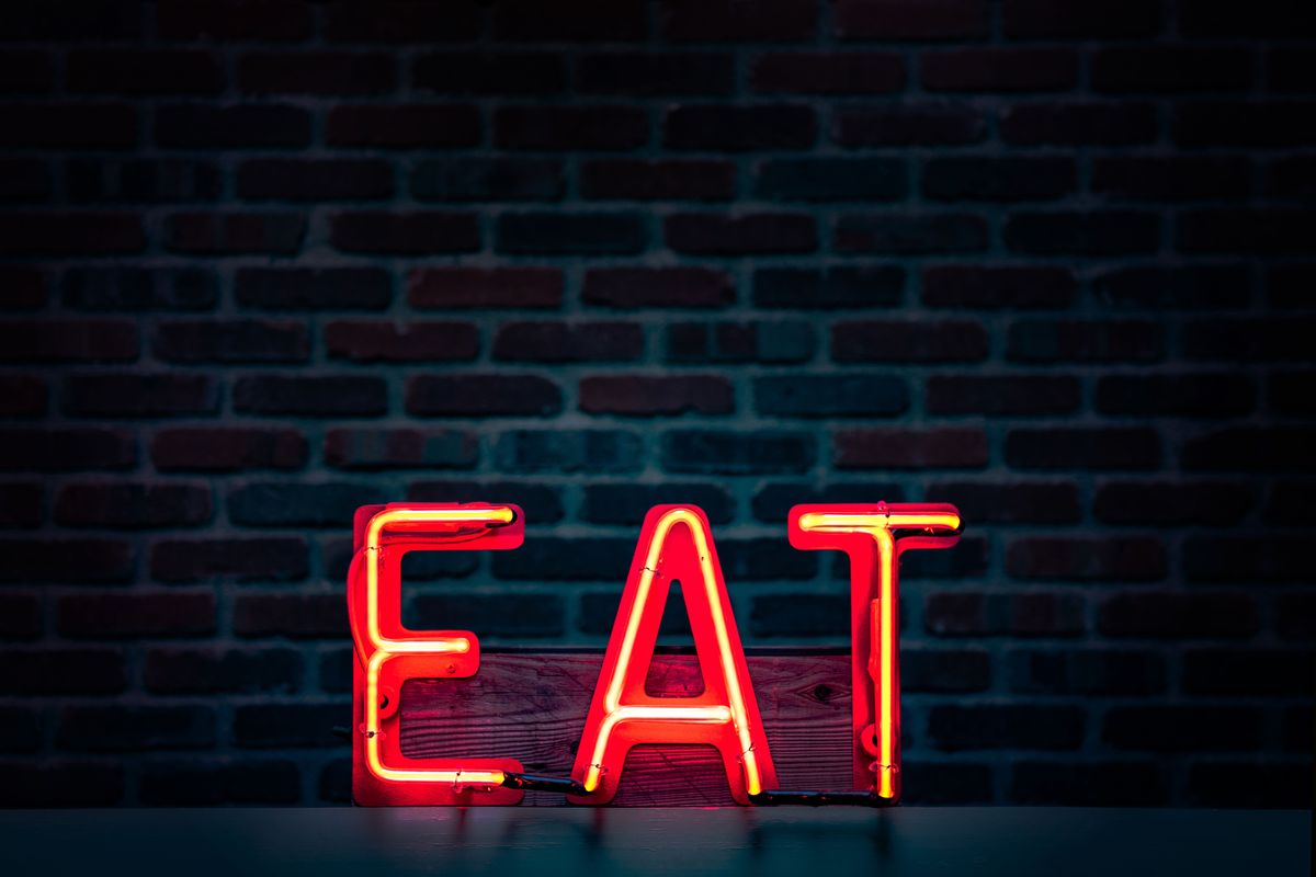 A red neon sign spelling EAT on a dark brick wall.