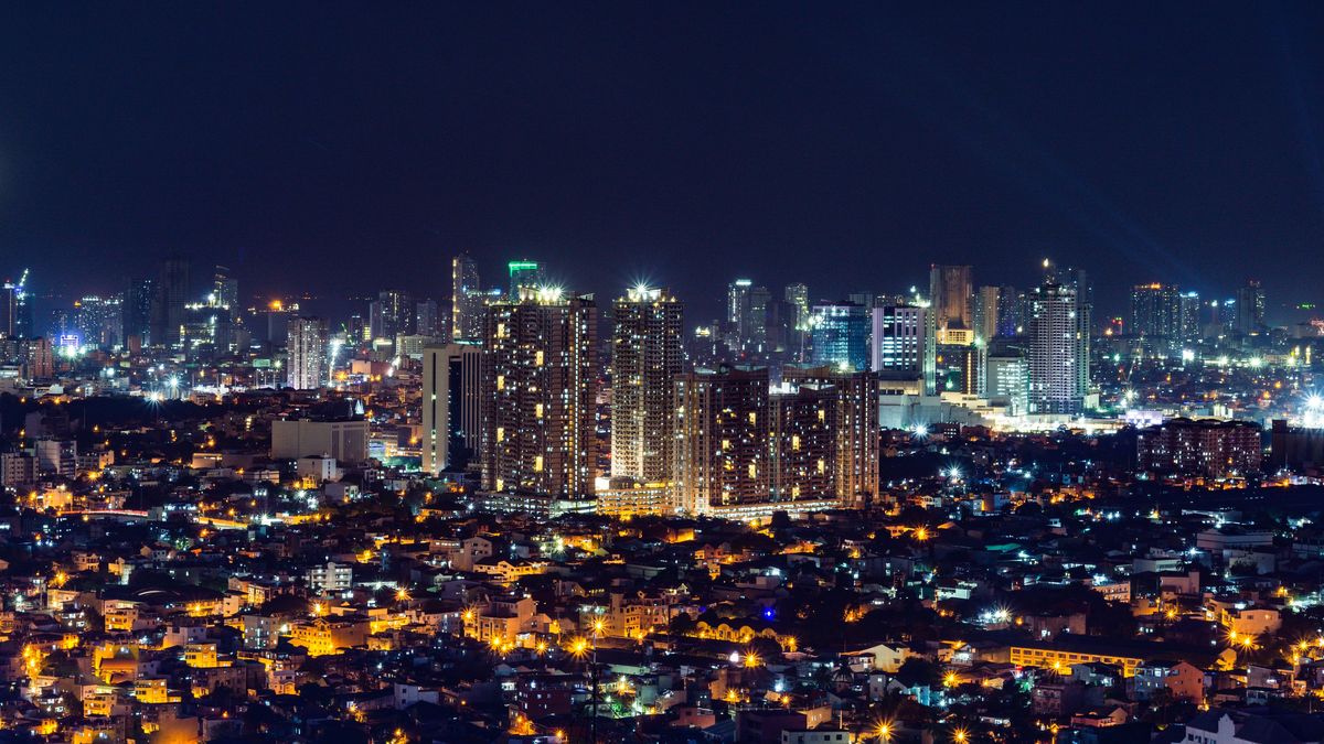 Metro Manila at night: warm streetlights across low-rise neighbourhoods, with lit towers in the middle distance.