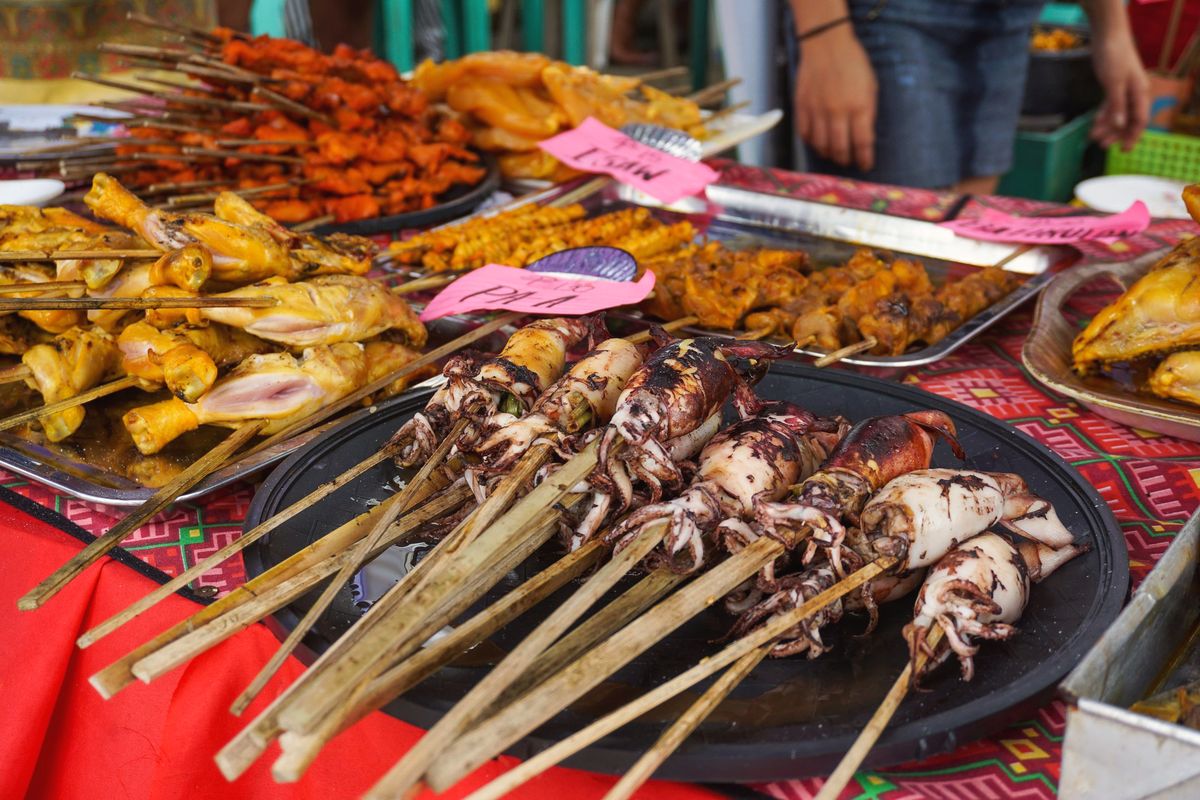 Grilled squid on bamboo skewers at a market stall, with handwritten pink price cards.