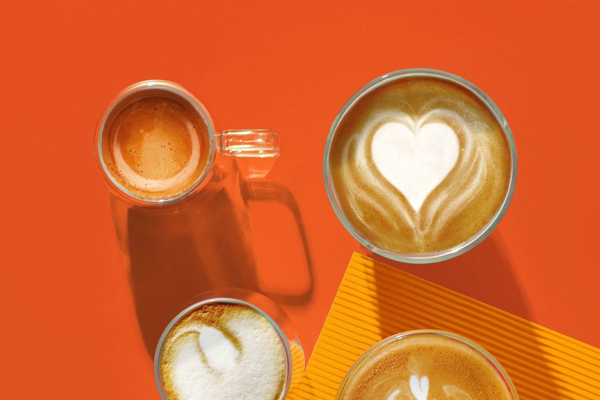 Four glass coffees seen from above, two with latte art, on a red-orange and yellow background.