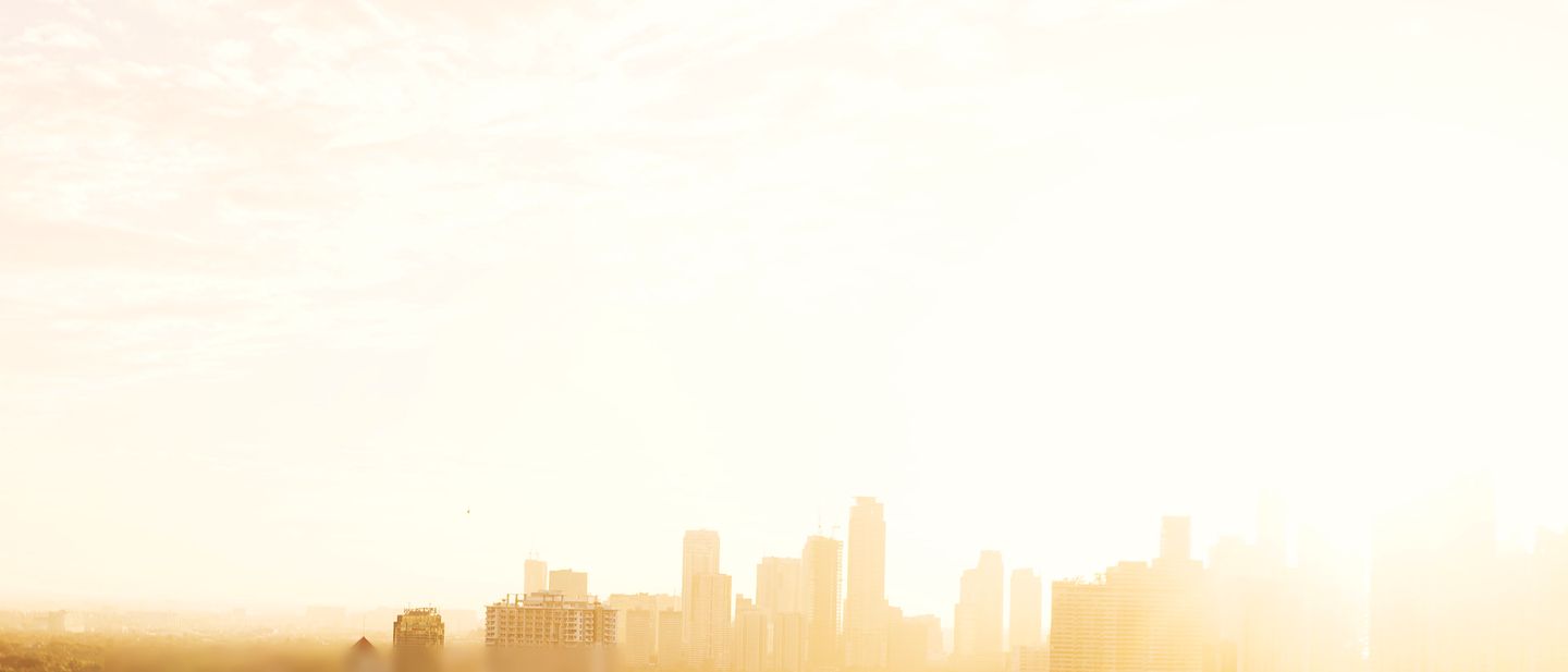 A hazy city skyline at sunrise, backlit by the sun.