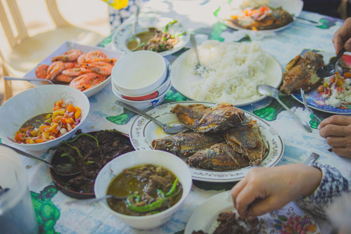 A home table with fried fish, rice, shrimp and soup, with hands reaching in from the edges.