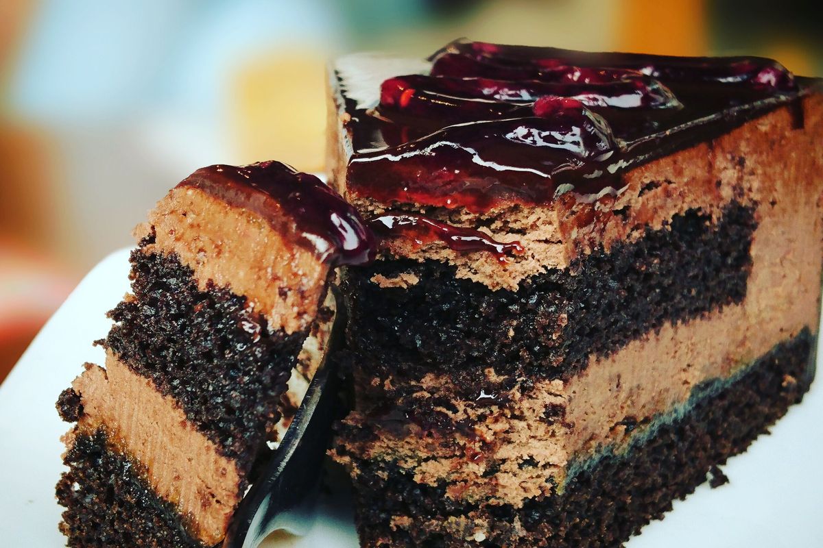 A slice of layered chocolate cake with a glossy berry topping on a white plate.