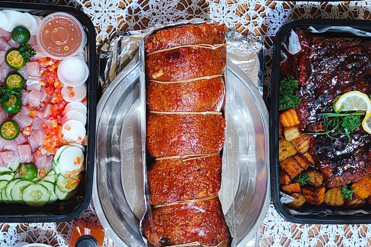 A party spread seen from above: rolled lechon belly in the centre, surrounded by trays of fried chicken, pancit, kinilaw and glazed ribs.