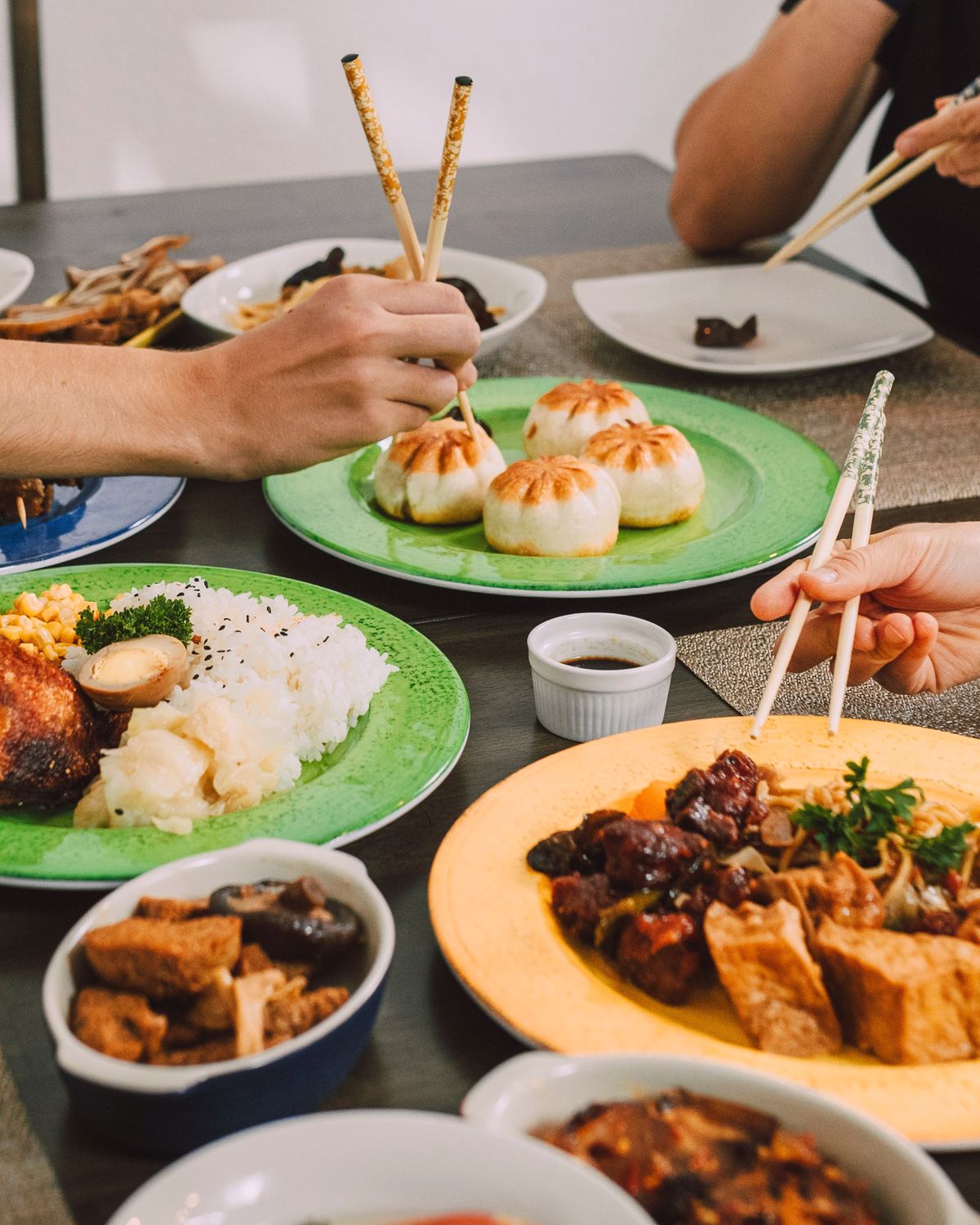 Chopsticks reaching into shared plates of buns, rice and braised meat.