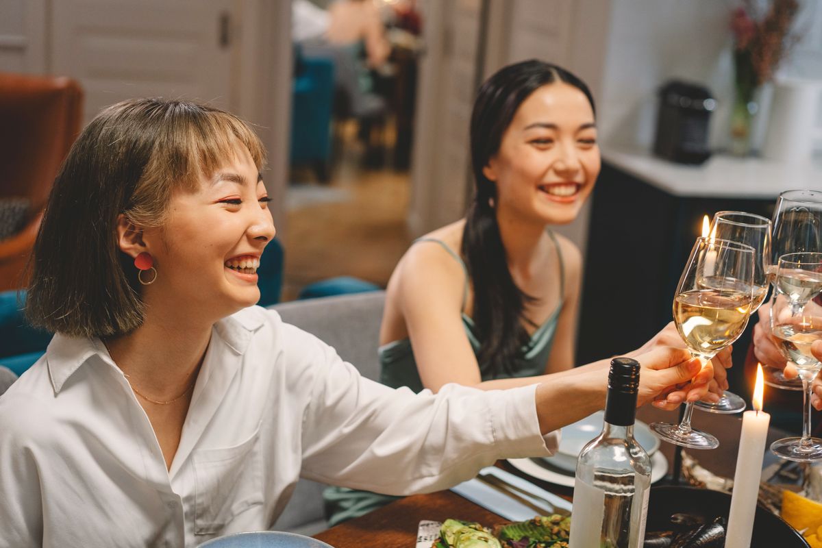 Two friends laughing as they clink wine glasses at a candlelit dinner table.