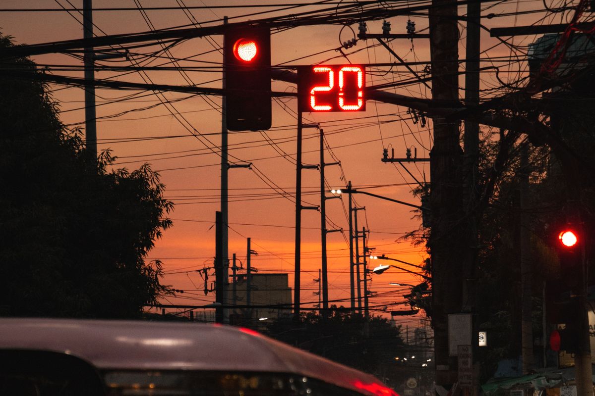 A red traffic light with a glowing 20-second countdown above a jeepney, under tangled power lines at dusk.